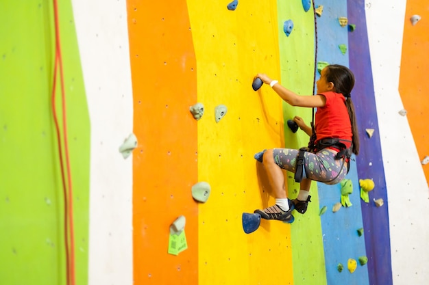 Menina esportiva escalando pedra artificial em uma parede prática no ginásio