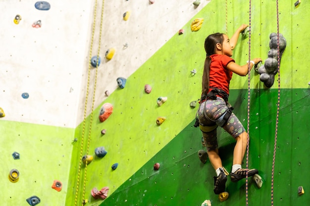 Menina esportiva escalando pedra artificial em uma parede prática no ginásio