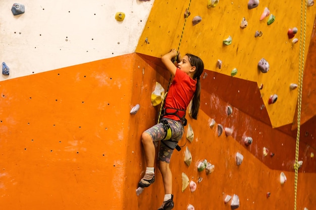 Menina esportiva escalando pedra artificial em uma parede prática no ginásio