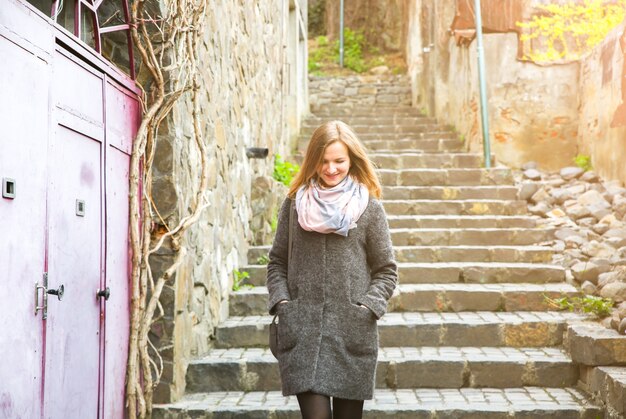 Menina está andando na rua estreita com calçada de pedra. Mulher elegante com uma bolsa de couro. Escadas da cidade.