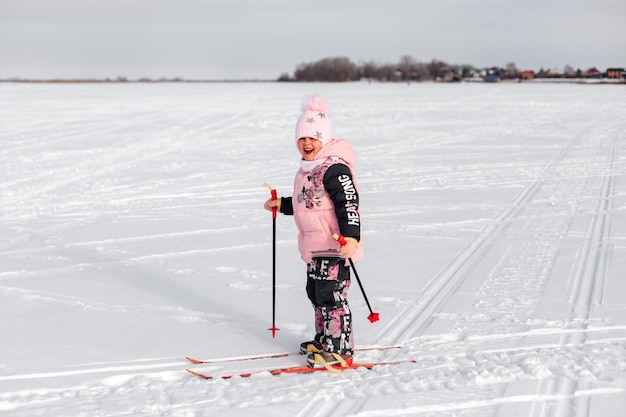 Menina está esquiando menina feliz de terno rosa aprende a esquiar ela posa na estrada de neve no fundo...