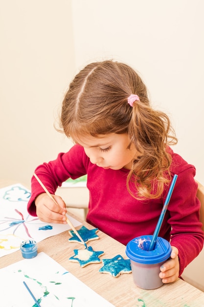 Menina está pintando com um pincel e aquarelas em figuras de argila. Decorações natalinas feitas à mão