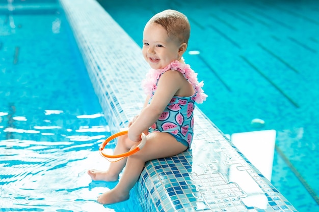 Menina está rindo na piscina em uma aula de natação.