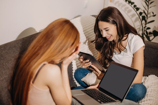 menina está usando um computador e sorrindo para sua amiga morena