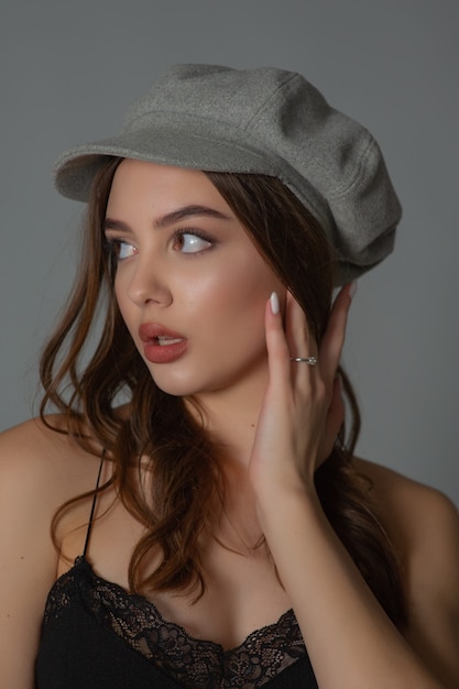 Foto menina estendeu a mão em um vestido preto e um boné cinza. linda garota com cabelos castanhos. retrato