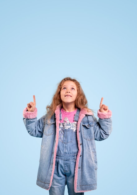 Foto menina estilosa em roupa jeans apontando para cima