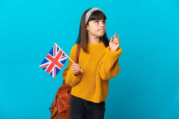 Menina estudando inglês isolada em um fundo azul com os dedos se cruzando e desejando o melhor