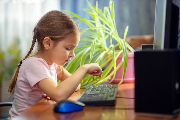 Menina estudante está sentado em casa em uma mesa de computador e está envolvido em um computador desktop.