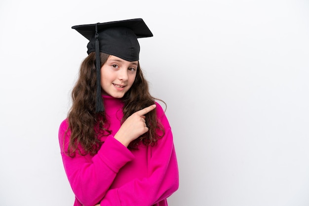 Menina estudante usando um chapéu graduado isolado no fundo rosa, apontando para o lado para apresentar um produto