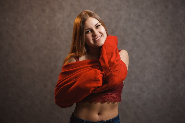 Menina experimentando um suéter vermelho em um fundo cinza