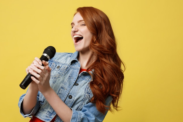 Menina expressivo que canta com um microfone, fundo amarelo brilhante isolado.