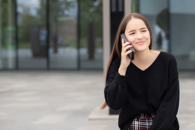 Menina falando em um smartphone ao lado de um escritório moderno, sorrindo