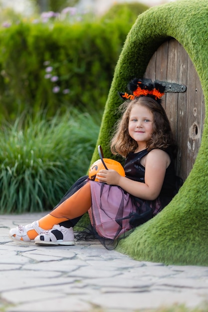 menina fantasiada de bruxa para o Halloween caminha no parque em uma cesta de doces