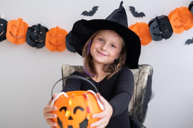 menina fantasiada de bruxa segurando abóbora com doces, comemorando o Halloween em casa