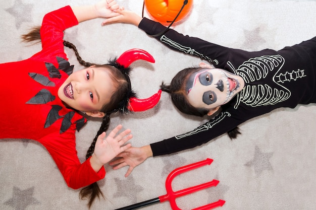 Menina fantasiada de carnaval de halloween com jack o lanterna (abóbora) e tridente. As crianças fofas asiáticas se provocam alegremente.