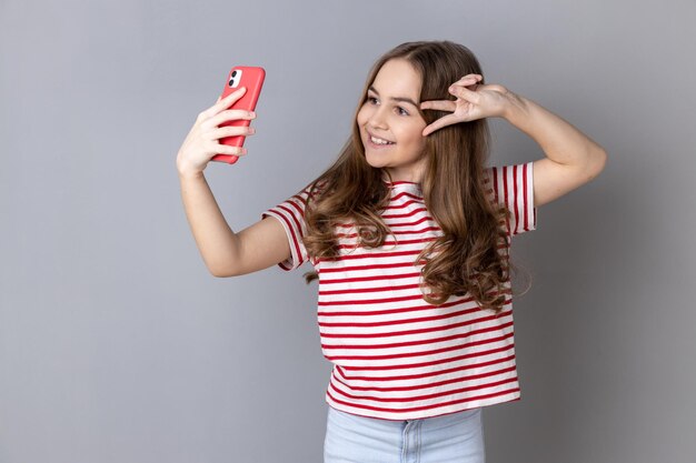 Menina faz sinal de paz na câmera de poses de celular para fazer selfie ou videochamada