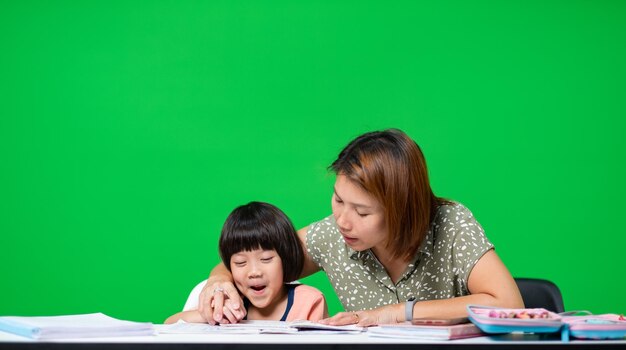 menina fazendo lição de casa com a mãe na tela verde criança escrevendo o conceito de educação de papel de volta à escola
