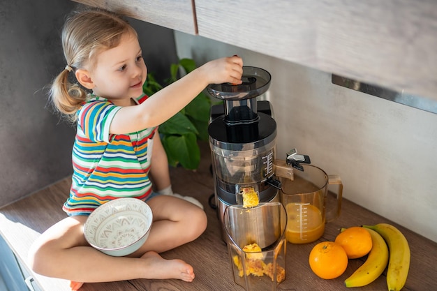 Menina fazendo suco fresco sentado em cima da mesa na cozinha de casa