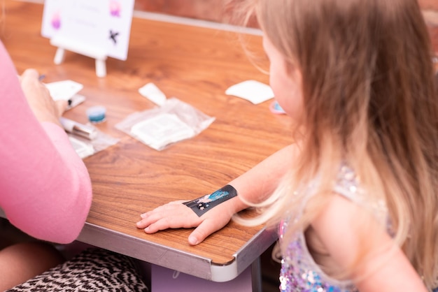 Menina fazendo tatuagem de glitter na festa de aniversário