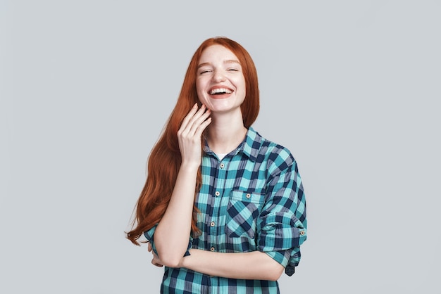 Menina feliz, alegre e despreocupada com um lindo cabelo ruivo comprido rindo em pé sobre um fundo cinza