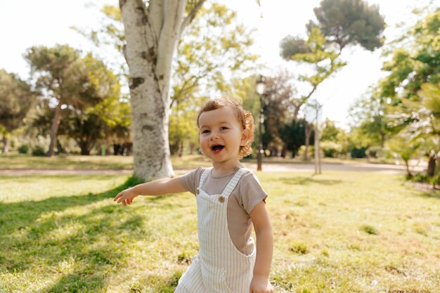 Menina feliz animada com cachos vestindo terno de verão e camiseta mostrando o dedo em direção ao parque ensolarado