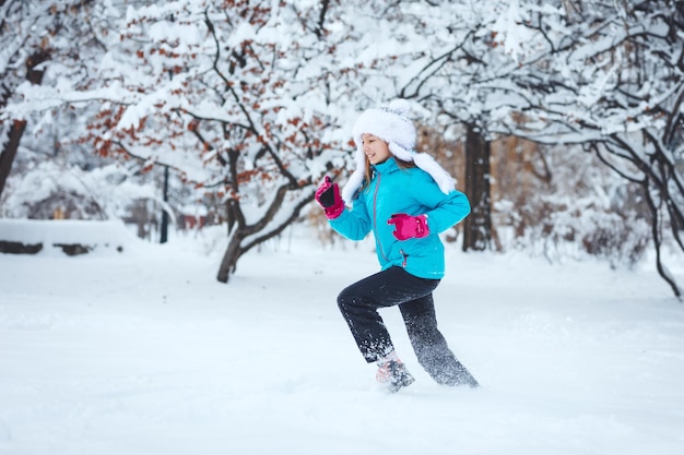 Menina feliz bonitinha com roupas de inverno está se divertindo correndo em dia de inverno nevado.