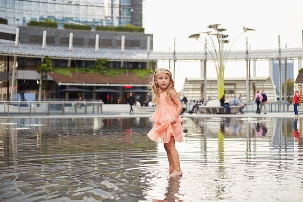 Menina feliz brincando com água em uma fonte na praça