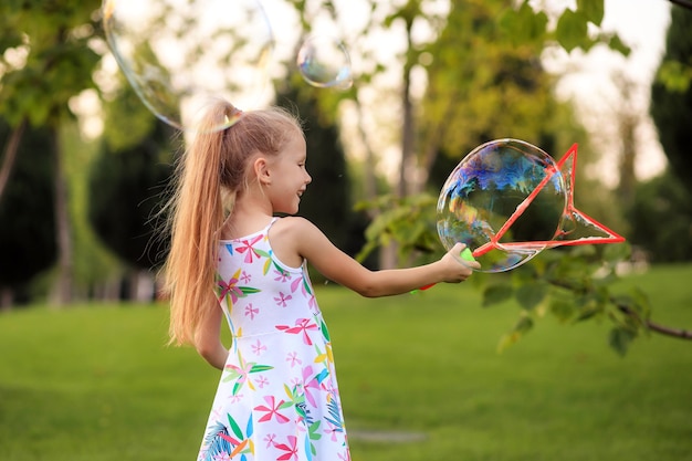 Menina feliz brincando com bolhas de sabão de verão no parque.