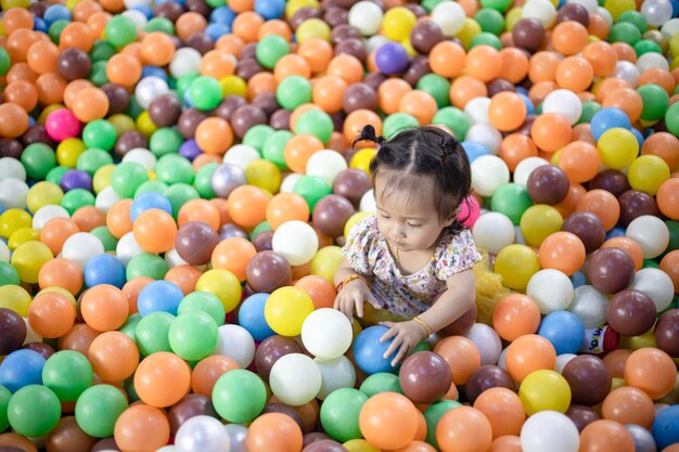 Menina feliz brincando na bola colorida Bebê em bolas de plástico multicoloridas