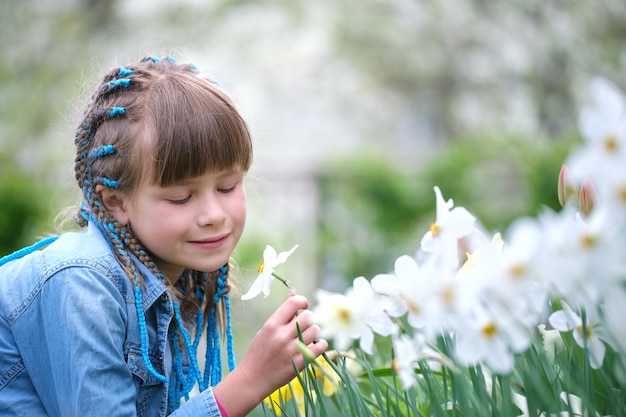 Menina feliz brincando no jardim de verão desfrutando do doce aroma de flores brancas de narciso em dia ensolarado