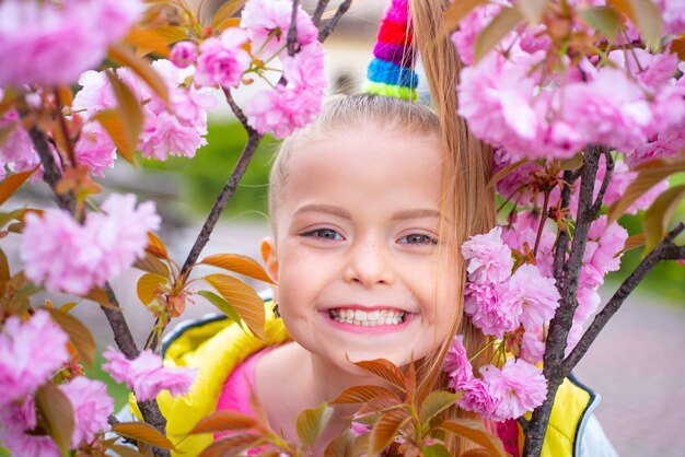 Menina feliz brincando sob a cerejeira em flor com flores cor de rosa, festival da flor de cerejeira de sakura