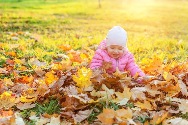 Menina feliz brincando sob folhas amarelas caindo no belo parque de outono na natureza caminha ao ar livre Criança vomita folhas de bordo laranja de outono Olá conceito de outono