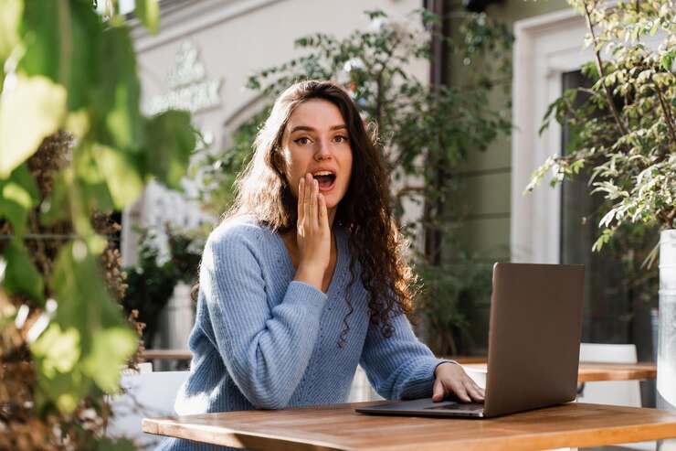 Menina feliz chocada se alegra em ganhar a aposta e sentada com o laptop ao ar livre no café Sorriso alegre de mulher surpresa e olhando para a quantidade de ganhos no cassino online e se alegra