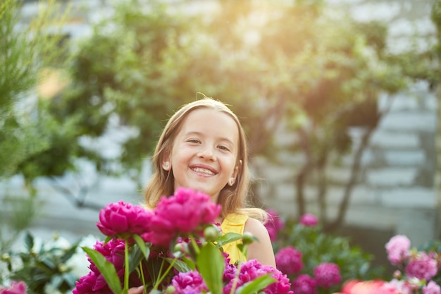 Menina feliz com aparelho no jardim em arbustos de peônias