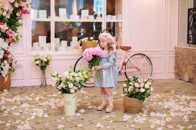 Menina feliz com cabelo encaracolado em um vestido e uma boina segurando um buquê de flores rosa ao ar livre