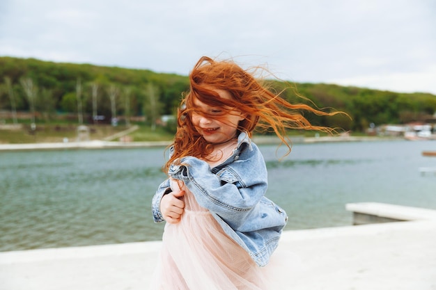 Menina feliz com cabelo vermelho corre ao longo da praia criança na praia