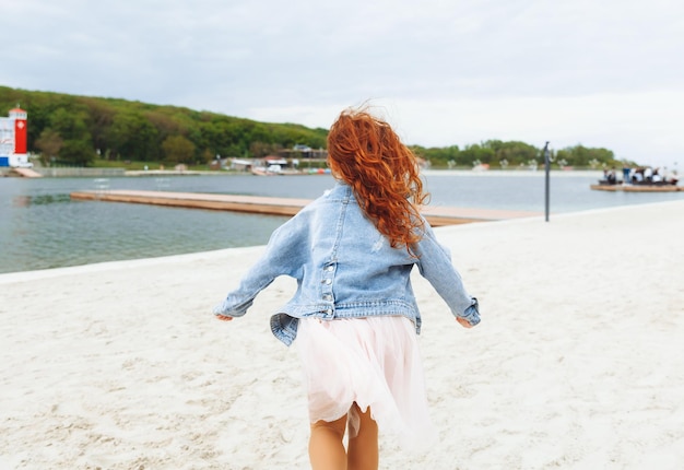 Menina feliz com cabelo vermelho corre ao longo da praia criança na praia