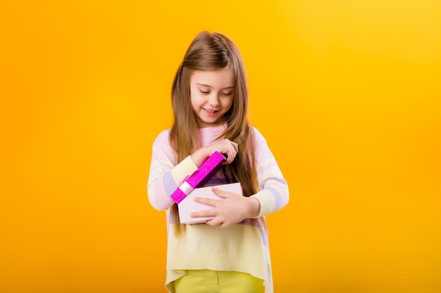 Menina feliz com cabelos longos, segurando uma caixa de presente rosa em um espaço amarelo isolado