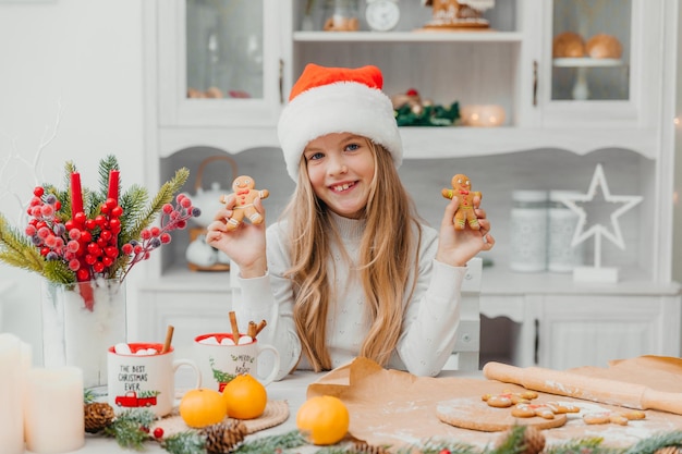 Menina feliz com chapéu de Papai Noel mantém homens-biscoito de gengibre.