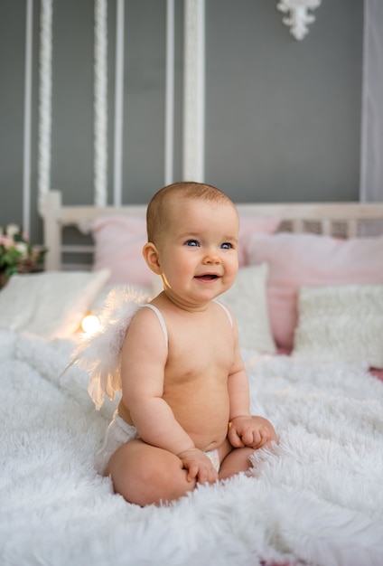 Menina feliz com fraldas e asas, sentada na cama