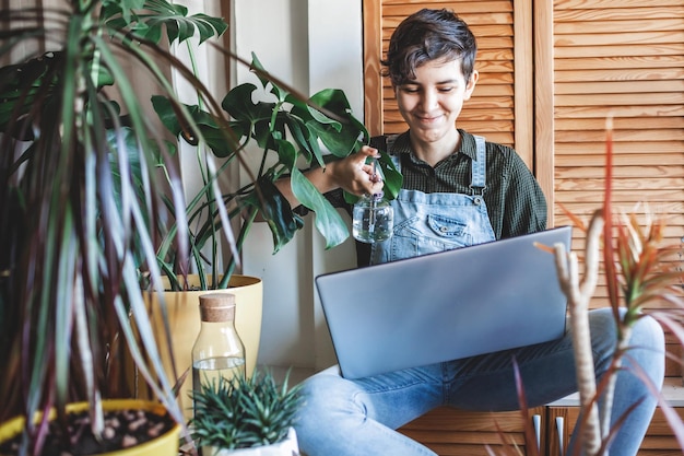 Menina feliz com laptop entre plantas no ambiente verde da varanda na jardinagem da sala