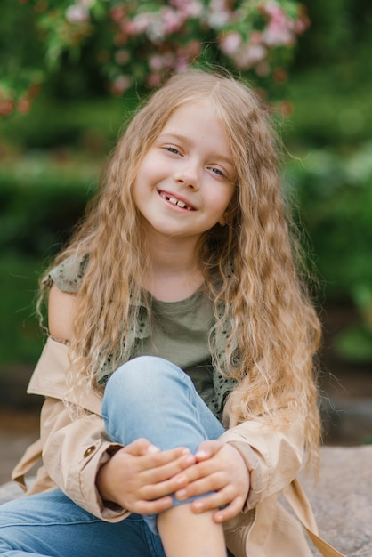 Menina feliz com longos cabelos castanhos ondulados senta-se em uma pedra na primavera em um parque florescente e sorri