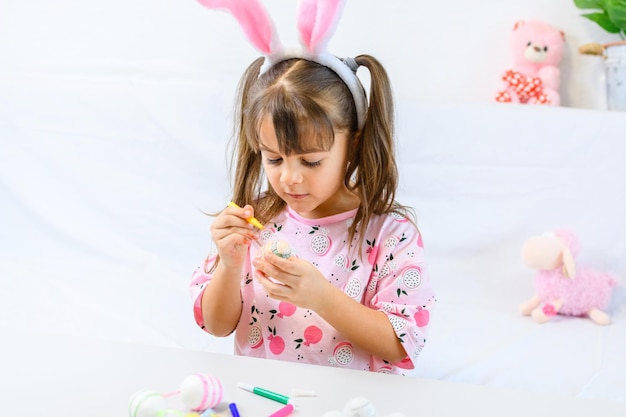 Menina feliz com orelhas de coelho pintando o ovo com fiberpen se preparando para o dia de Páscoa feliz