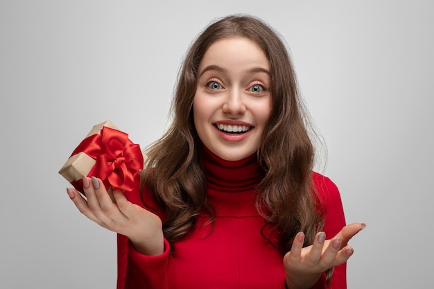 Menina feliz com um suéter vermelho segurando um presente com fita vermelha, presente no Natal ou Ano Novo