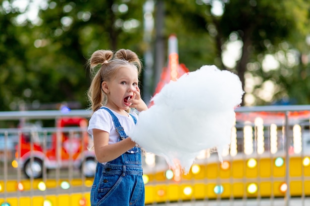 Menina feliz comendo algodão doce no parque de diversões no verão