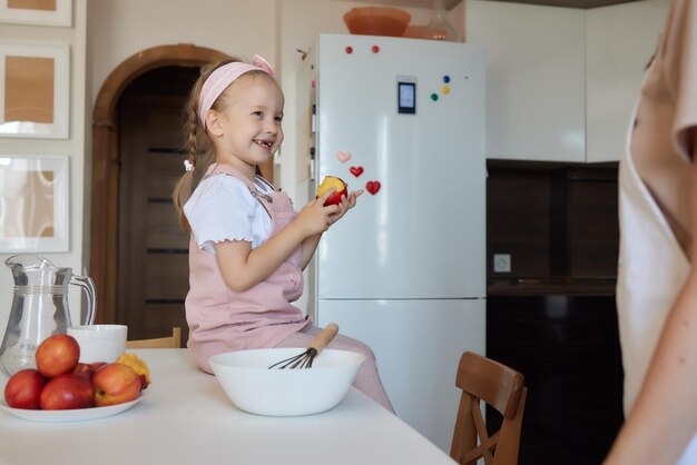 Menina feliz comendo frutas e bebendo água sentada à mesa na cozinha