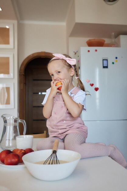 Menina feliz comendo frutas e bebendo água sentada à mesa na cozinha