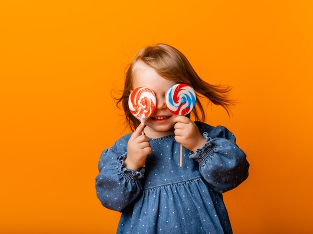 Menina feliz comendo pirulito grande, criança com doces. isolado no fundo brilhante, estúdio.