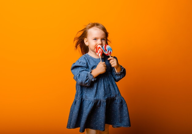 Menina feliz comendo pirulito grande, criança com doces. isolado no fundo brilhante, estúdio.