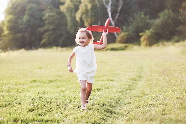 Menina feliz correndo no campo com um avião de brinquedo vermelho nas mãos